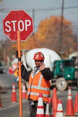 Traffic control flagger in high-visibility gear holding a stop paddle in a work zone